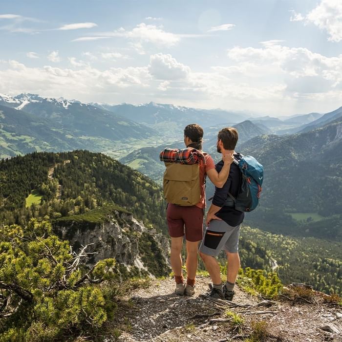 Two hikers with backpacks overlooking a mountainous landscape near Falkensteiner Hotels & Residences