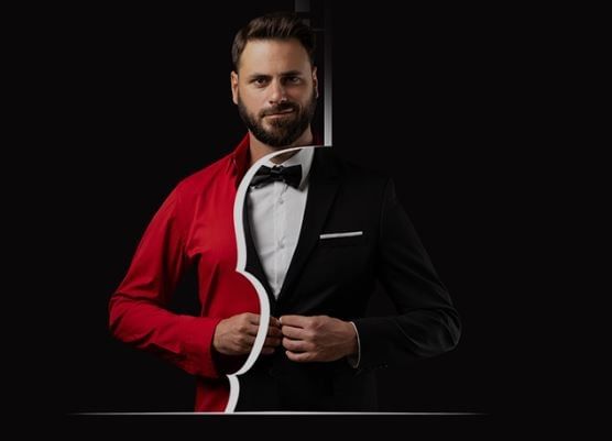 Portrait of Hauser in a symbolic composition – half dressed in a formal tuxedo, half in a red shirt – set against a black background.