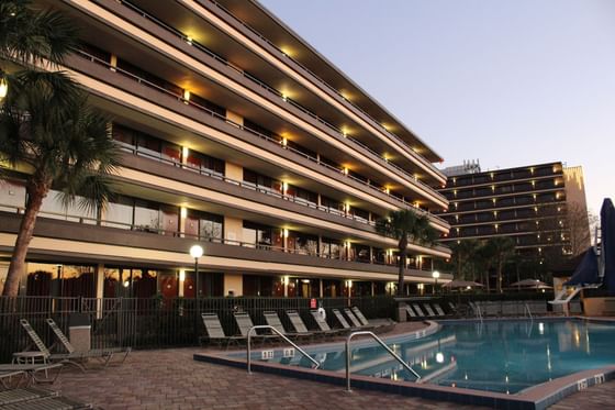 Outdoor swimming pool with deck chairs beneath illuminated hotel balconies and palm trees at Rosen Inn at Pointe Orlando