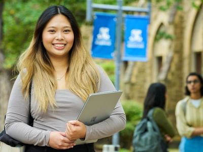 Smiling student holding a tablet with two other students in background at UniMelb across from Student Living - 800 Swanston.