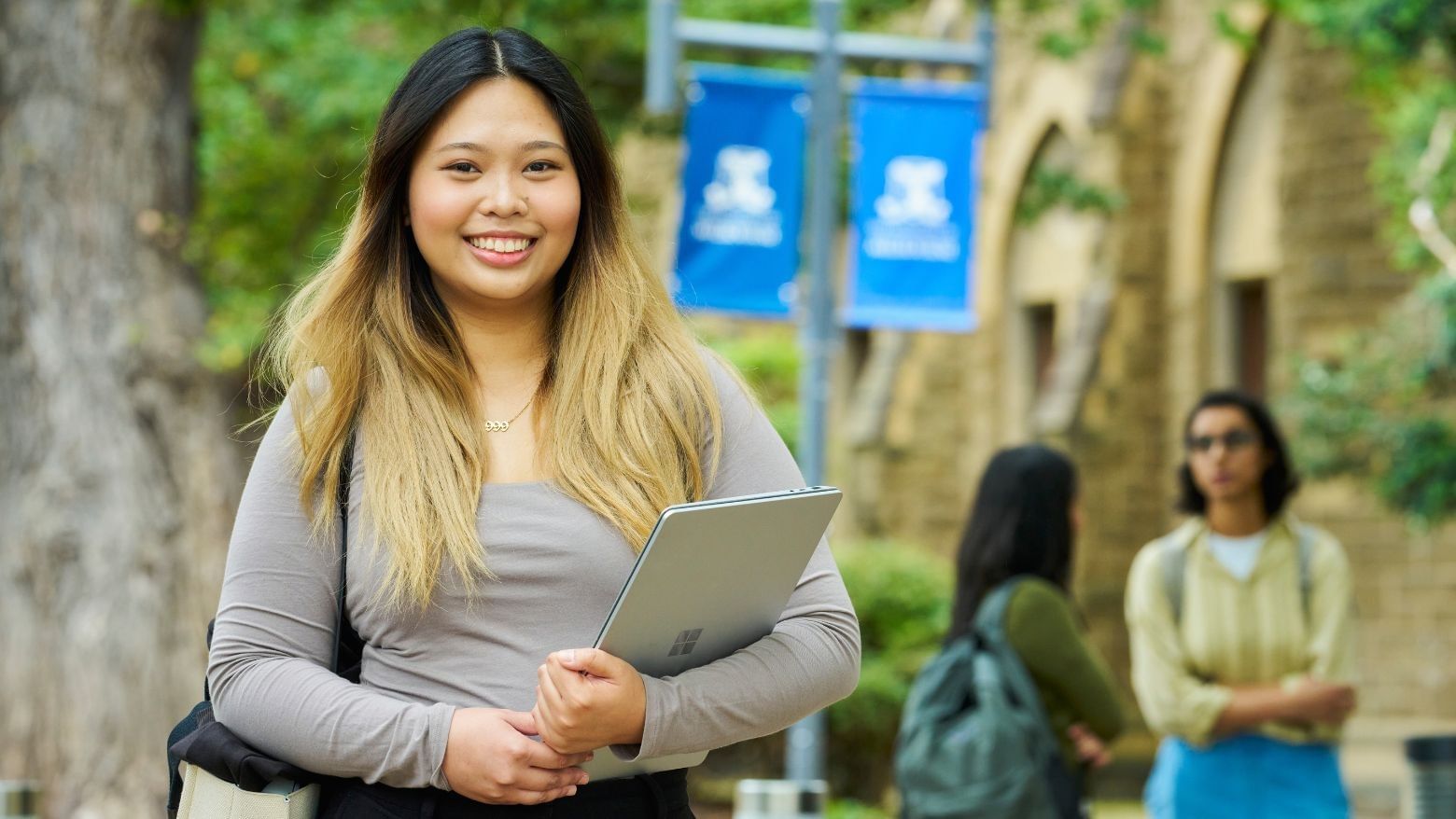 Smiling student holding a tablet with two other students in background at UniMelb across from Student Living - 800 Swanston.