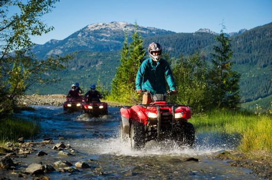 People riding ATVs through a stream near Blackcomb Springs Suites