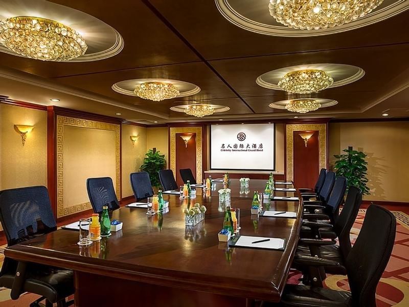 Set up a long wooden table facing the projector screen in the VIP Room 1 at Celebrity International Grand Hotel
