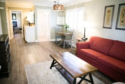 A cozy living room with red sofa, wooden coffee table, dining area with table and chairs, and two framed pictures on wall.