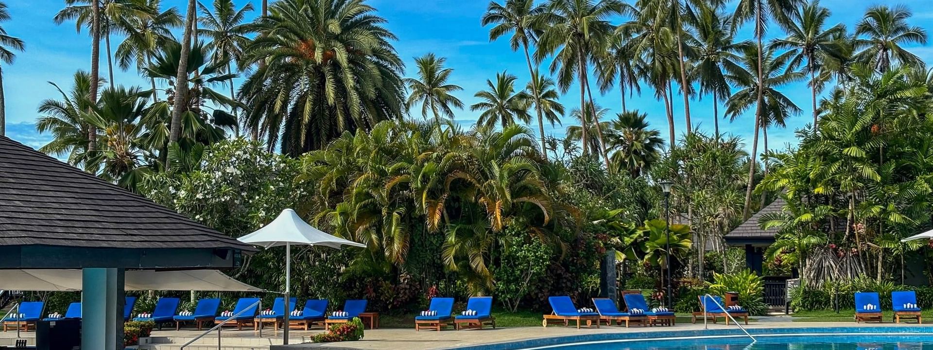 Blue pool with lounge chairs surrounded by tropical trees at The Naviti Resort in Korolevu