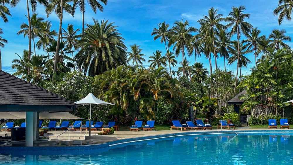 Blue pool with lounge chairs surrounded by tropical trees at The Naviti Resort in Korolevu.