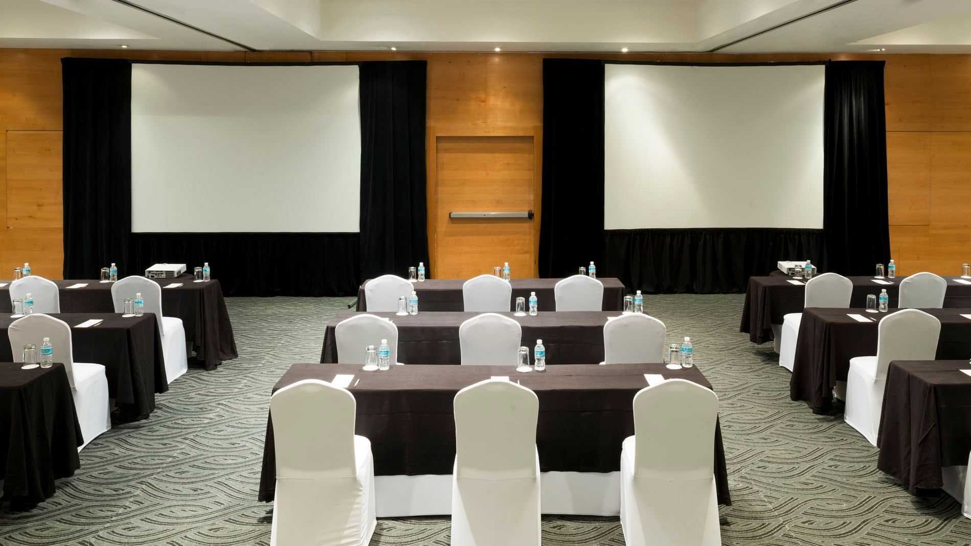 Large Nueva York Venue featuring multiple rows of tables and dual large projection screens at Real Inn Perinorte