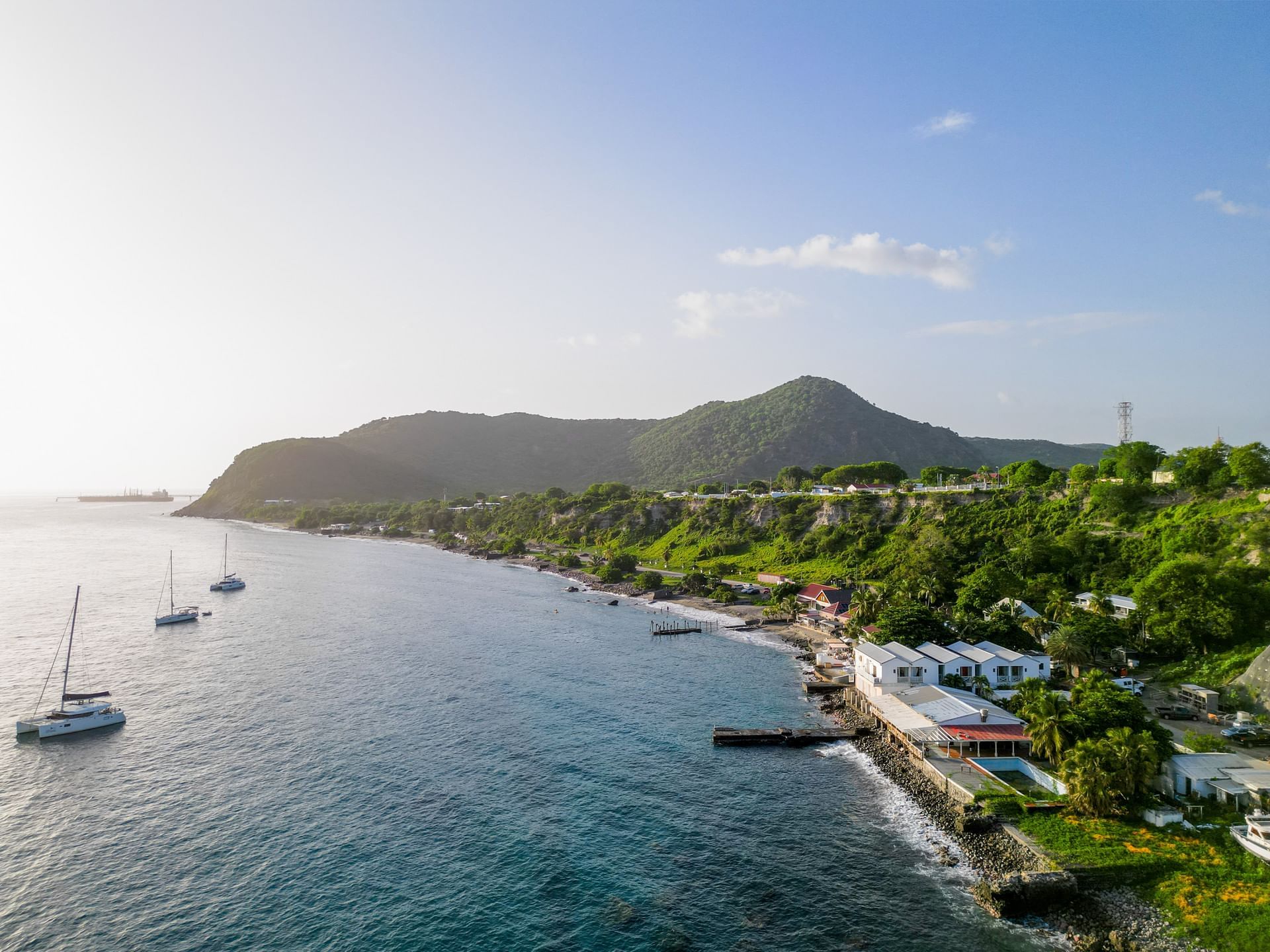 Luchtfoto van een rustig kustlandschap met zeilboten, groene heuvels en huizen aan het water nabij Golden Rock Resort