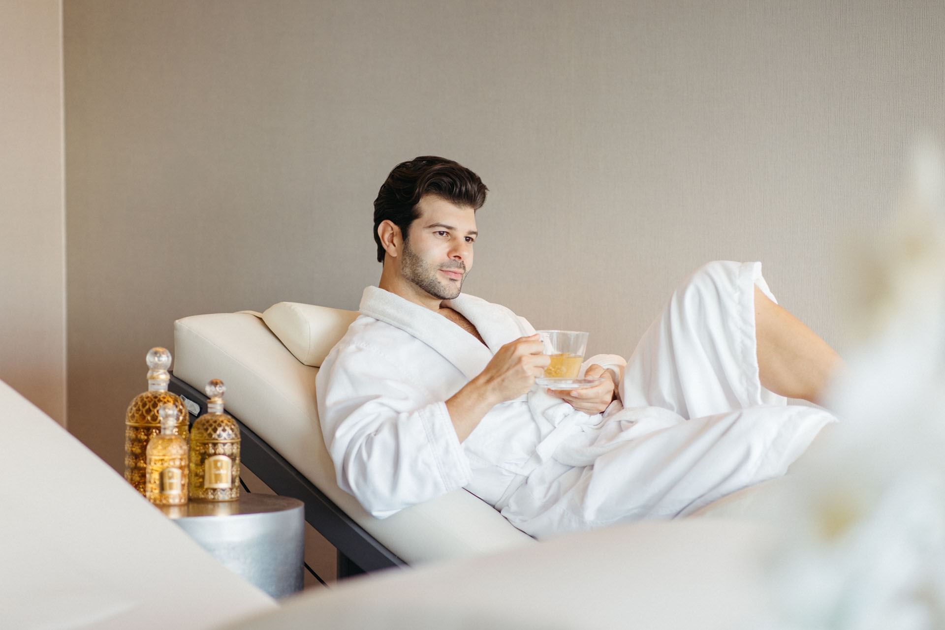 Man in a white bathrobe resting on a lounger while holding a glass cup of herbal tea at Guerlain Spa in Hotel X Toronto