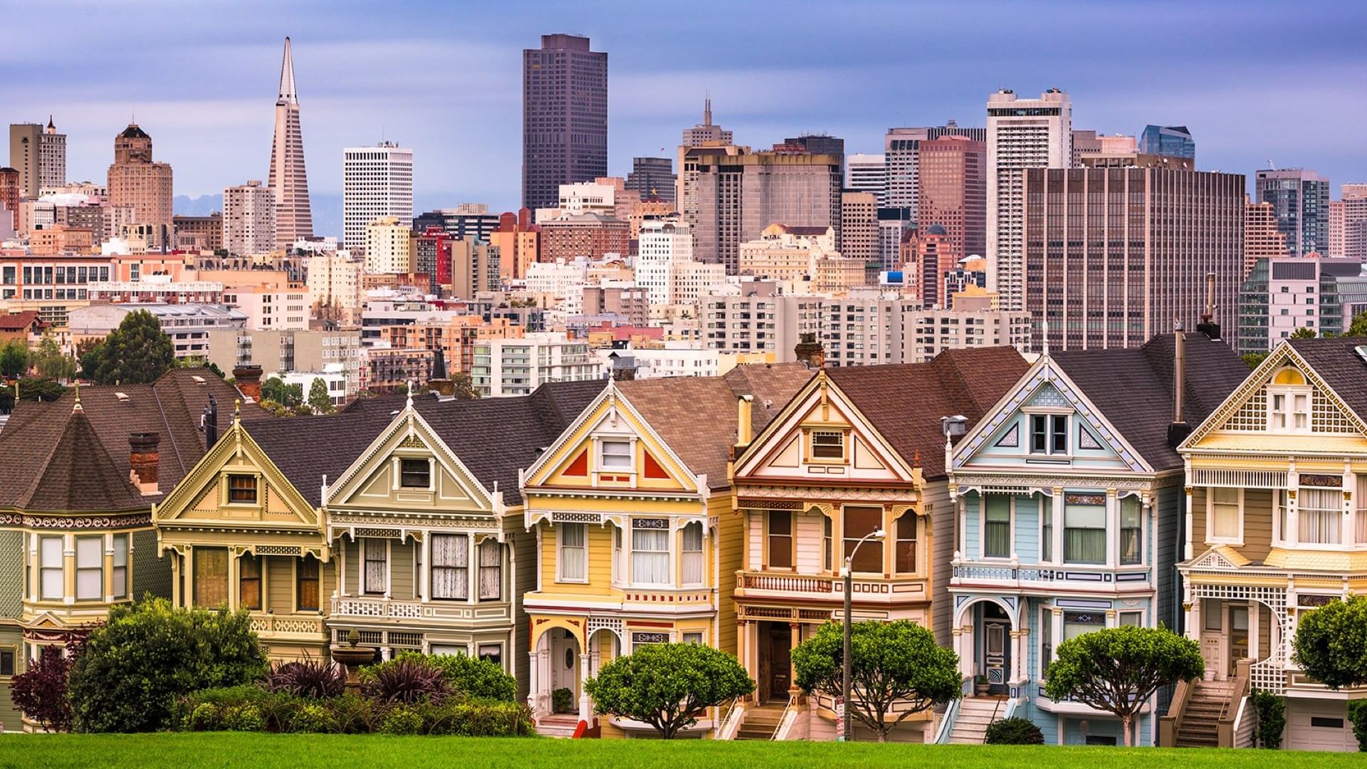 Colorful Victorian houses line a green lawn in front of the San Francisco skyline near Warwick Hotels and Resorts