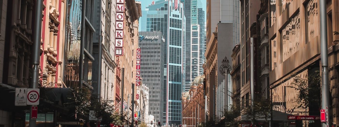 Sydney CBD street with tall buildings, tram tracks, and people walking near Novotel Sydney International Airport