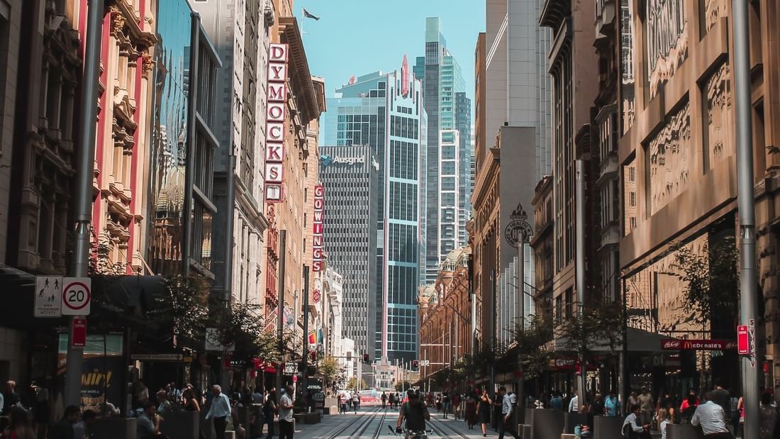 Sydney CBD street with tall buildings, tram tracks, and people walking near Novotel Sydney International Airport