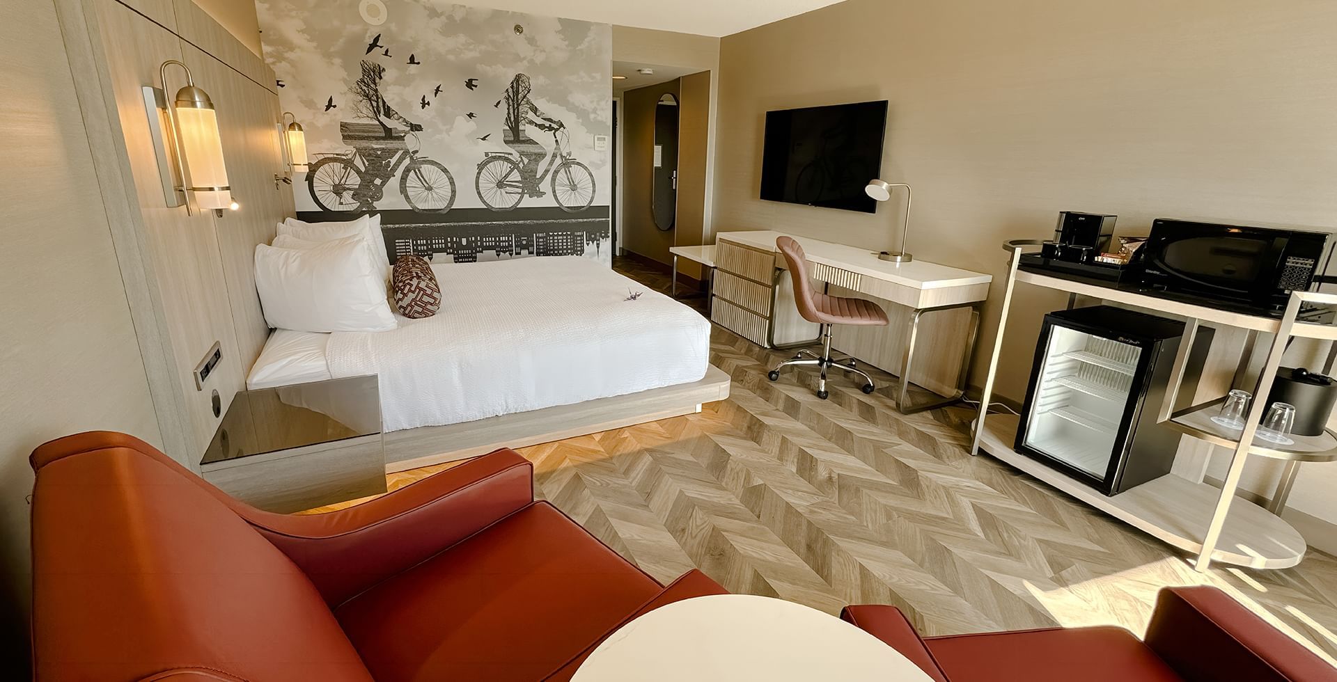 A hotel guestroom with king bed, couch, work desk, chair, flat screen TV, microwave and mini fridge