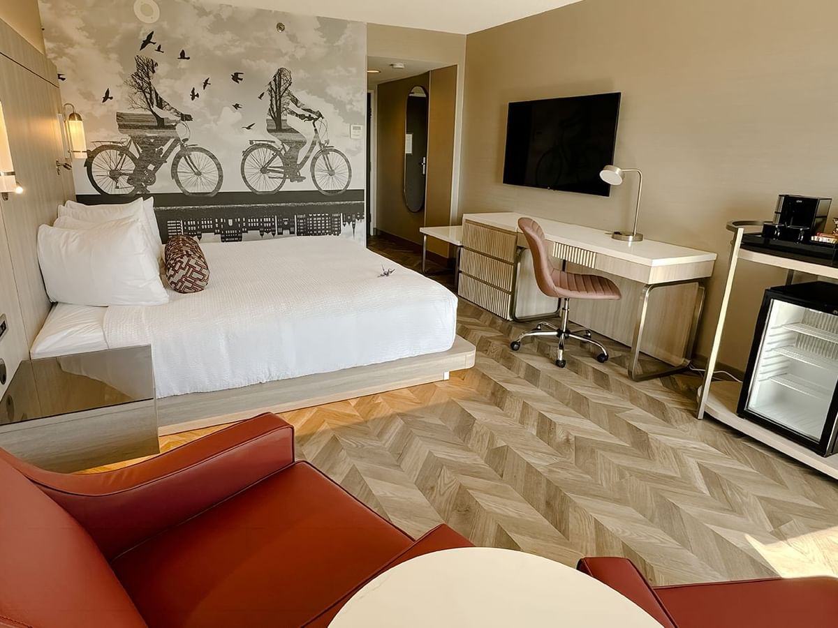 Hotel guestroom with King bed, sofas, work desk, TV, chair, mini fridge, and microwave.