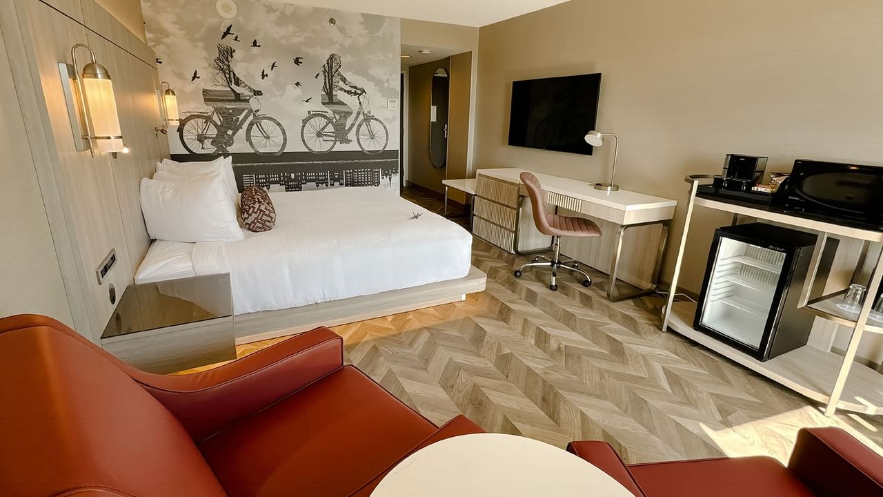 Hotel guestroom with King bed, sofas, work desk, TV, chair, mini fridge, and microwave.