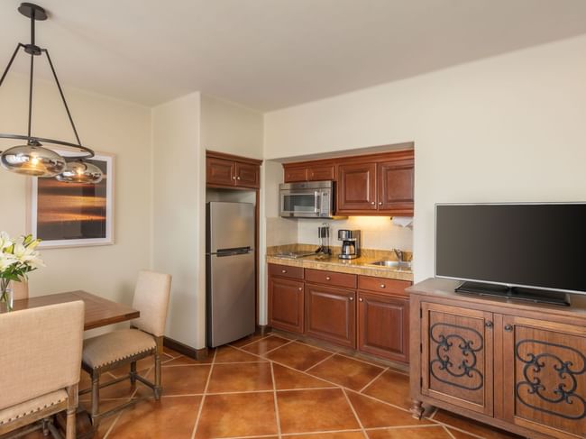 Dining space with wooden chairs beside a kitchenette and TV in Luxury Studios 2 Queen Beds at Hacienda Del Mar Los Cabos.