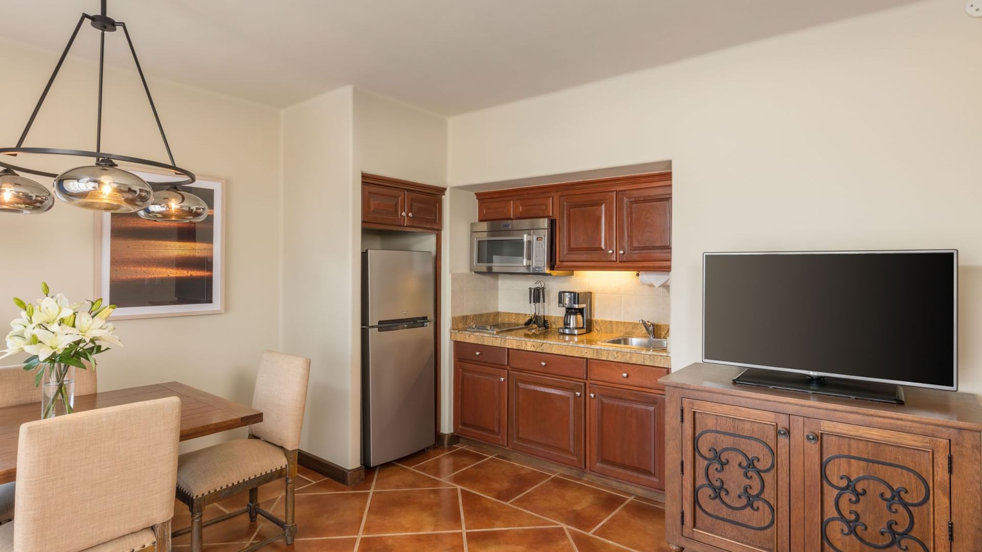 Dining space with wooden chairs beside a kitchenette and TV in Luxury Studios 2 Queen Beds at Hacienda Del Mar Los Cabos.