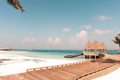Wooden walkway leads to a thatched pavilion over turquoise waters, surrounded by white sands at Ananea Madivaru Maldives