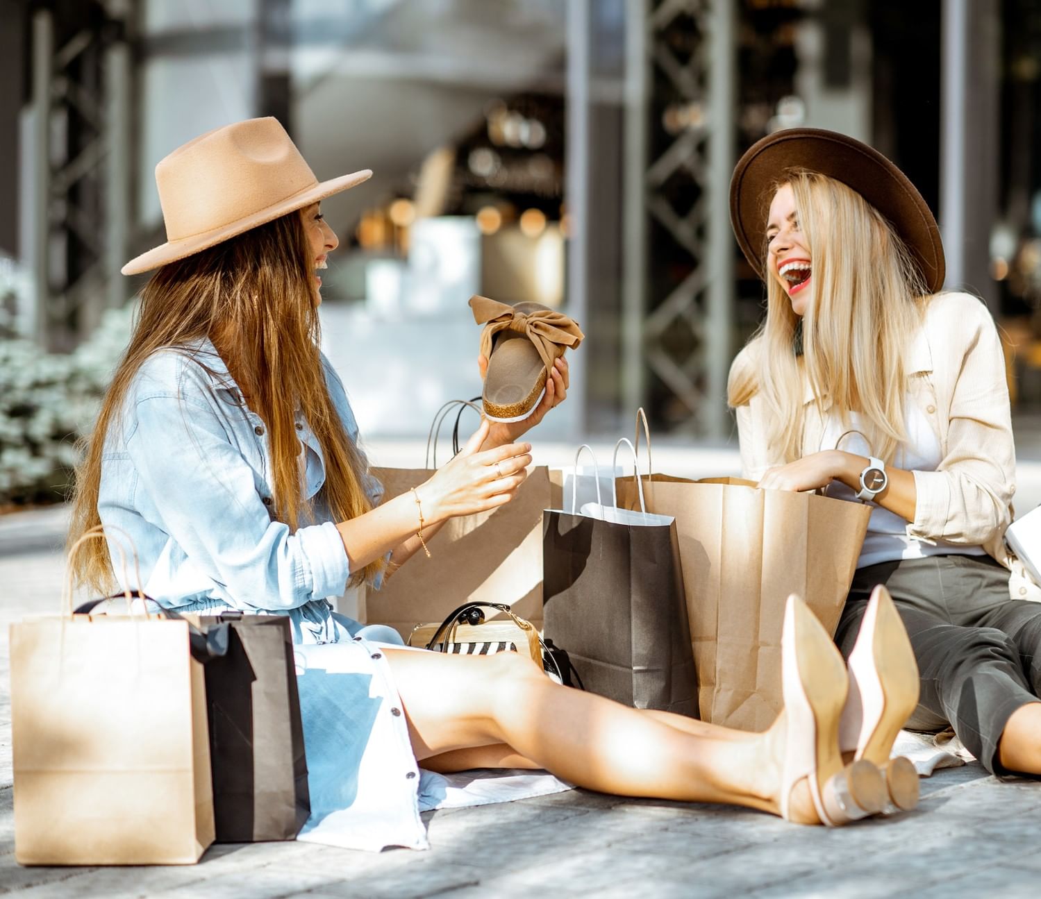 Two women laughing with shopping bags on the sunny outdoor patio of Hotel Barsey by Warwick