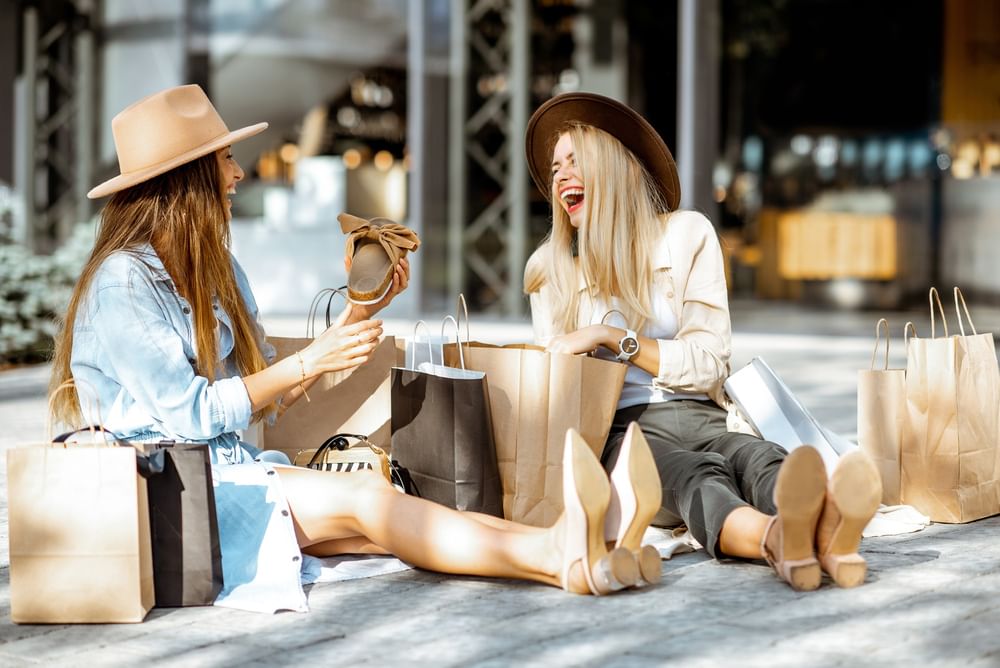 Two women laughing with shopping bags on the sunny outdoor patio of Hotel Barsey by Warwick