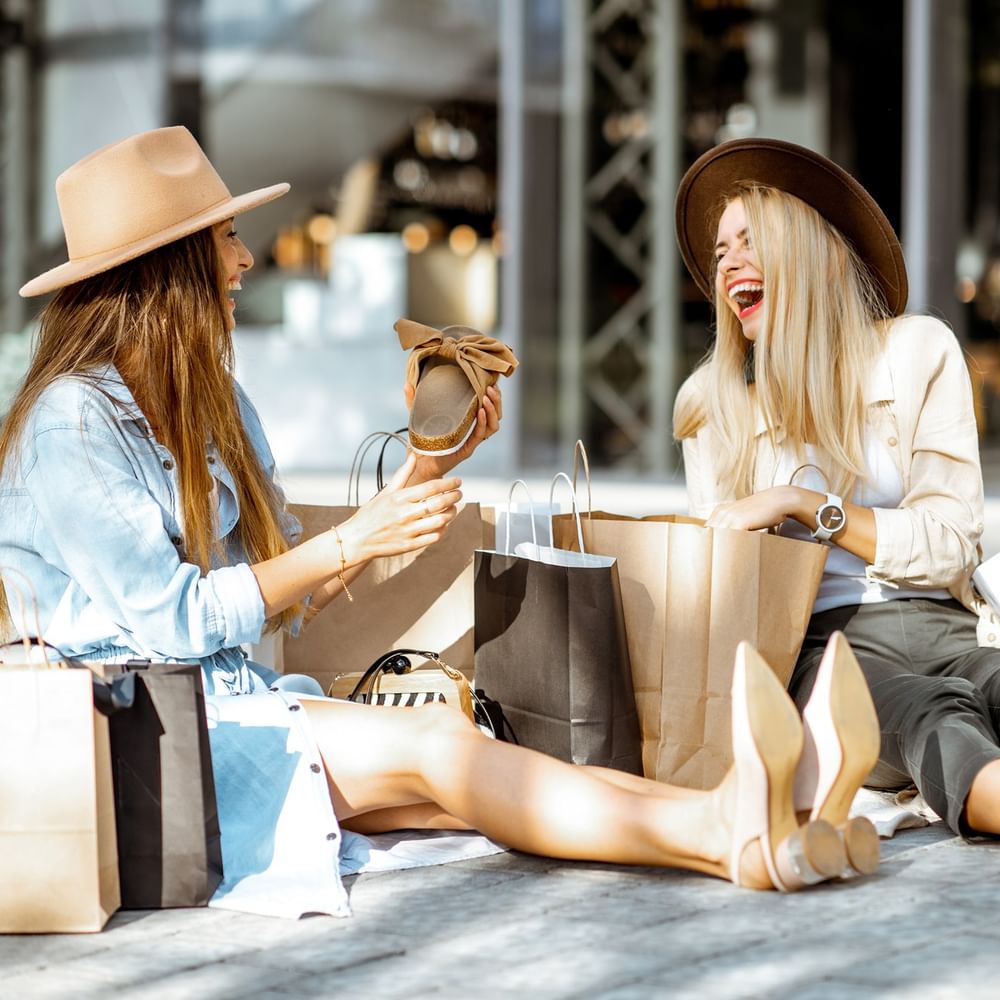 Two women laughing with shopping bags on the sunny outdoor patio of Hotel Barsey by Warwick