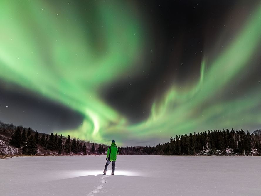Person standing in a snowy field watching the northern lights in Cold Lake