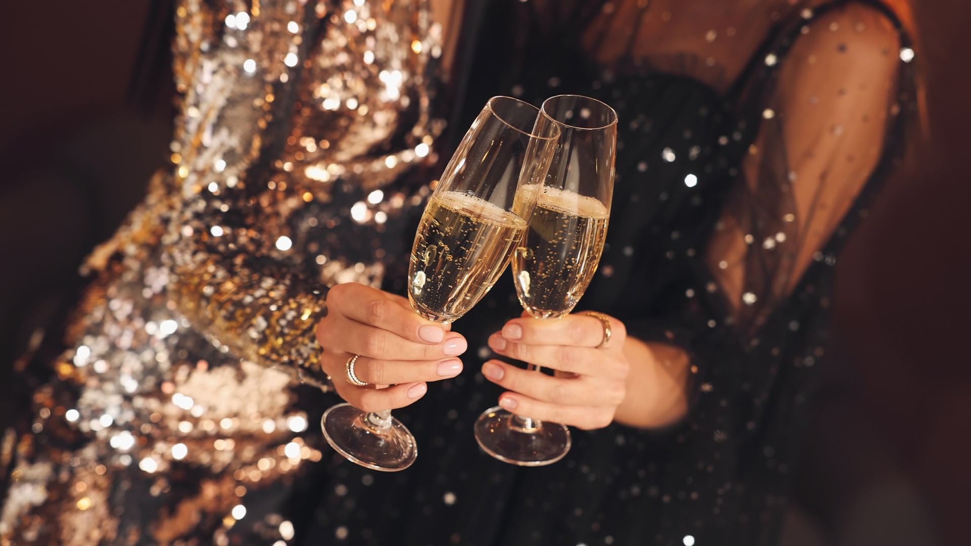 Zwei Frauen in glitzernden Kleidern stoßen mit Sektgläsern an.