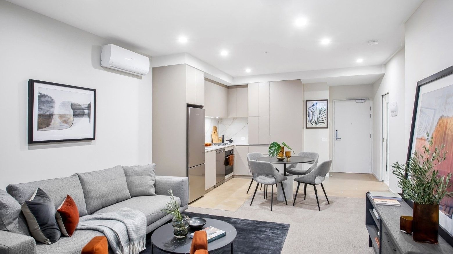 Modern living room with gray couch, dining area, and kitchen, featuring minimalist decor and neutral colors.