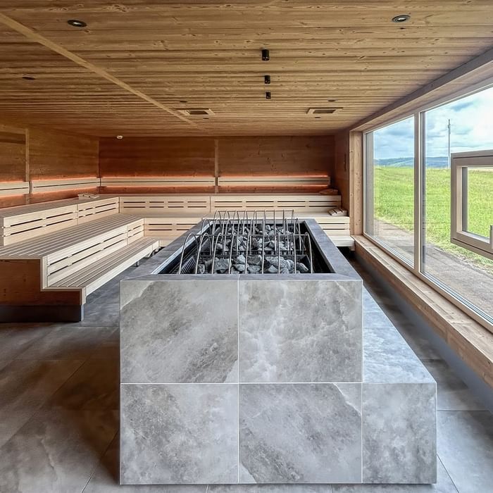 Holzsauna mit grauem Granitboden, großen Fenstern und Blick auf die grüne Landschaft.