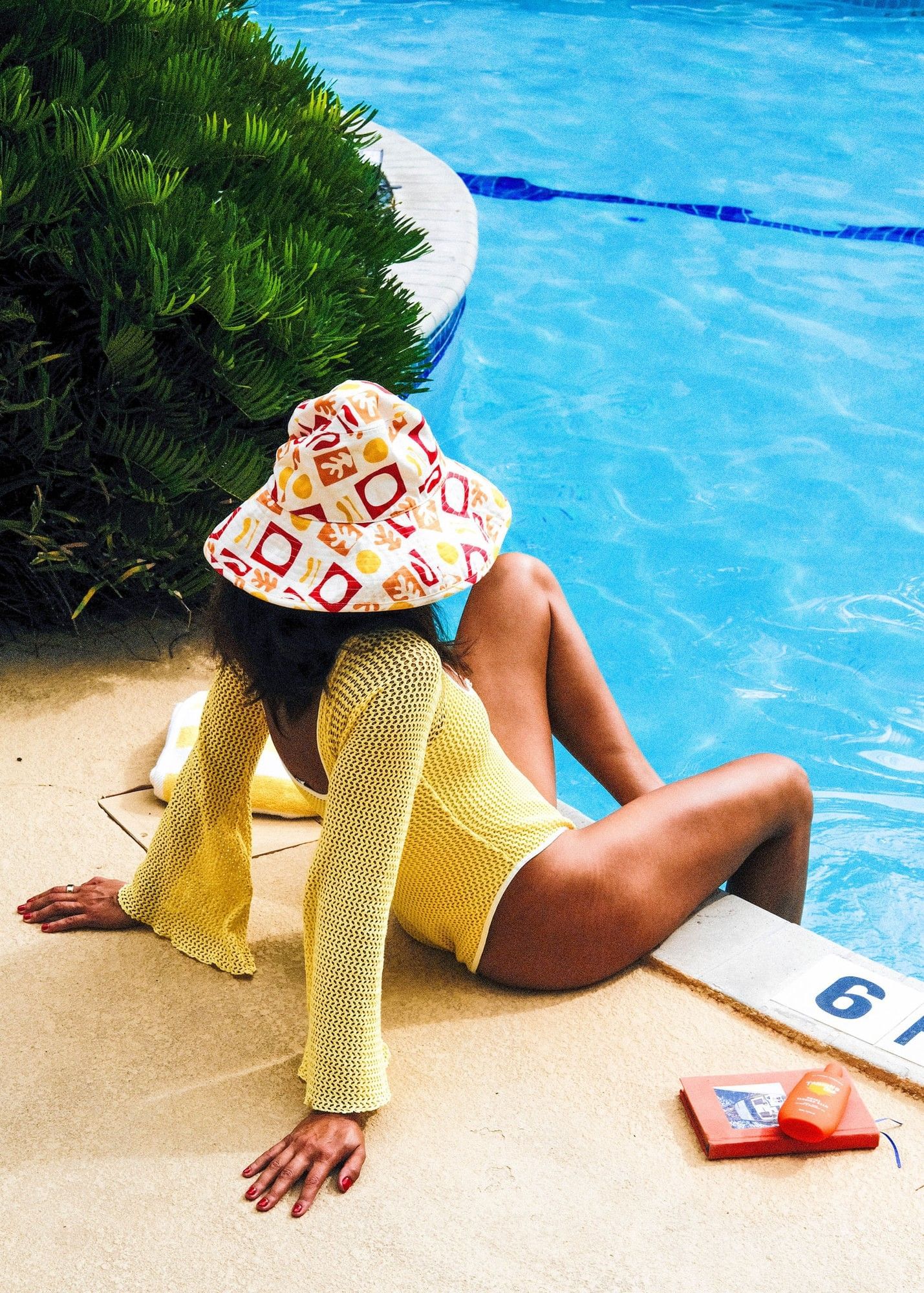 A woman in a yellow swimsuit and sunhat lounges by the pool.