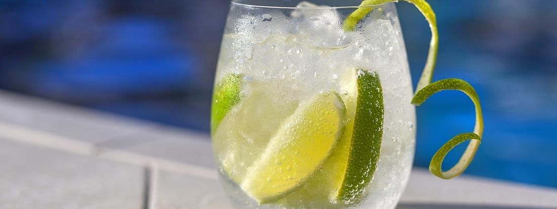 Iced cocktail with lime slices and a lime zest garnish sitting by a pool in Pool Grill & Bar at Warwick Le Lagon
