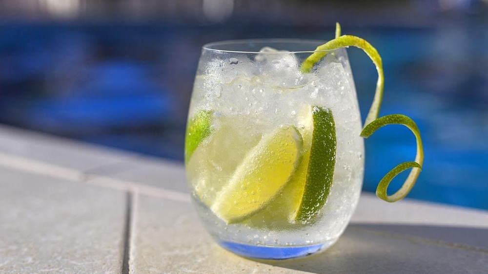 Iced cocktail with lime slices and a lime zest garnish sitting by a pool in Pool Grill & Bar at Warwick Le Lagon