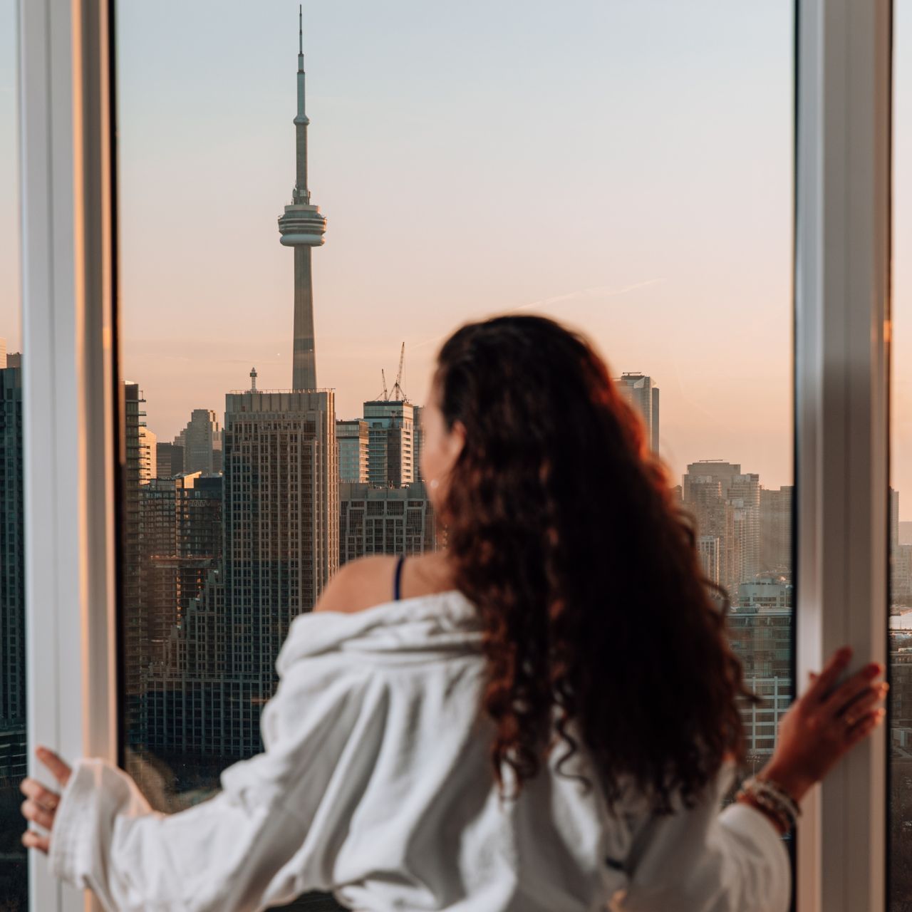 Woman in white robe standing by window with view of cityscape