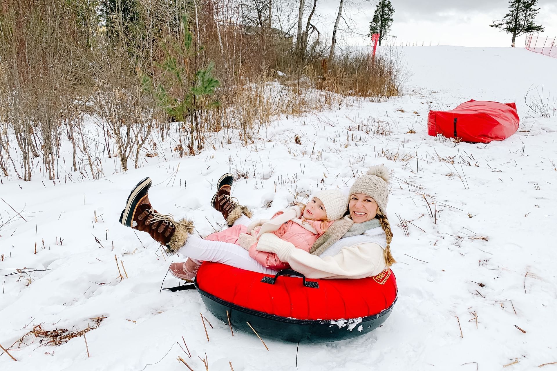 Mother and child riding a red snow tube down a hill, by snowy brush and trees at Mountain View Grand Resort & Spa