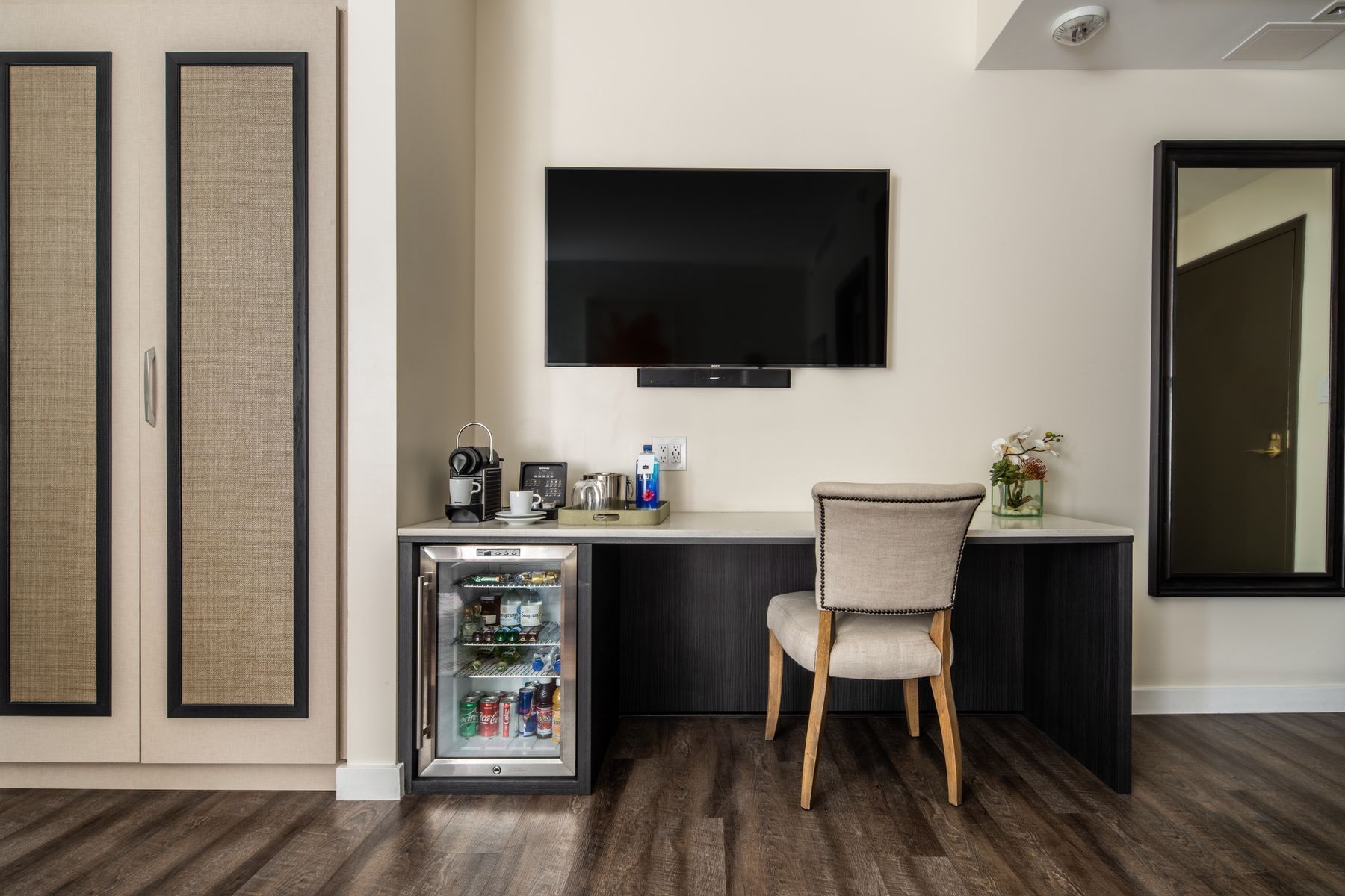 A hotel room with a desk, TV, mini-fridge, and chair.