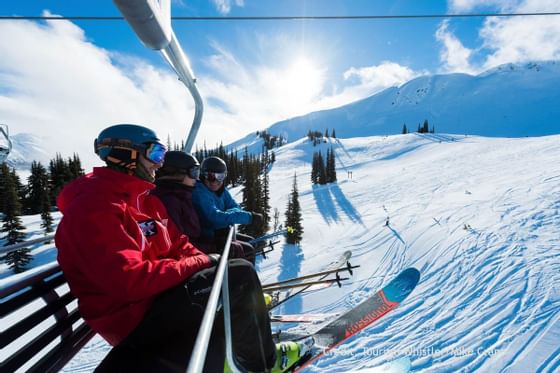 A group of people on a ski lift, surrounded by snow-covered mountains near Blackcomb Springs Suites