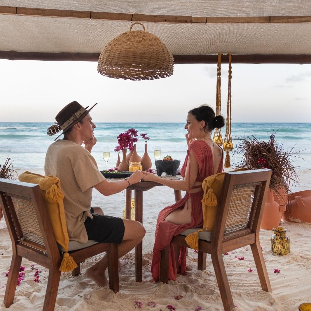 Romantic couple enjoying a private beachside dinner at La Zebra Hotel holding hands with ocean in background