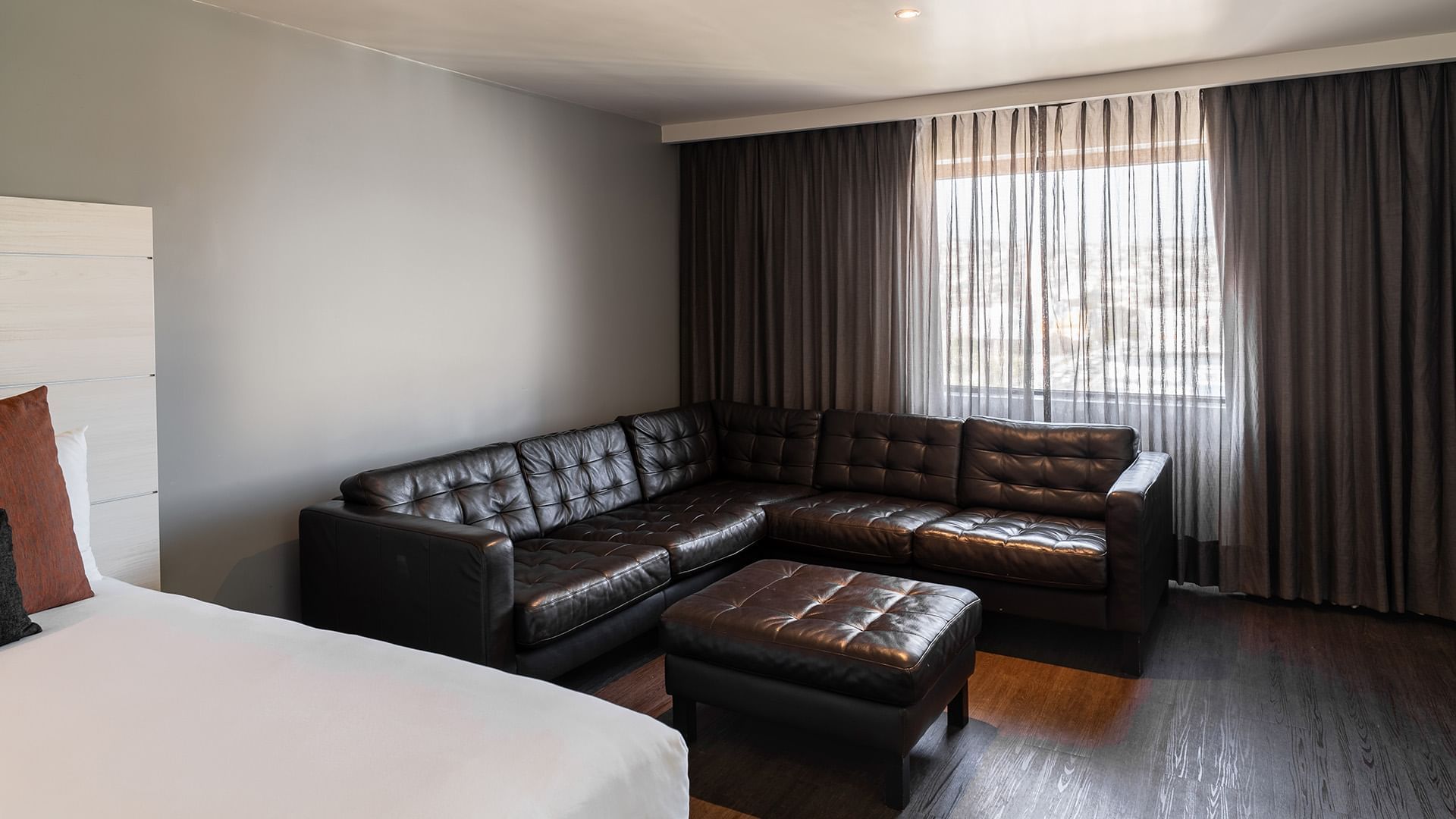 Tufted leather sofa and ottoman by the cozy bed in the Two Double Junior Suite with wooden floors at Real Inn Tijuana