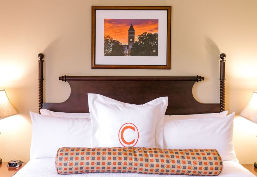 White king bed beneath a framed clock tower artwork in King Suite Lakeside at Clemson University Conference Center & Inn