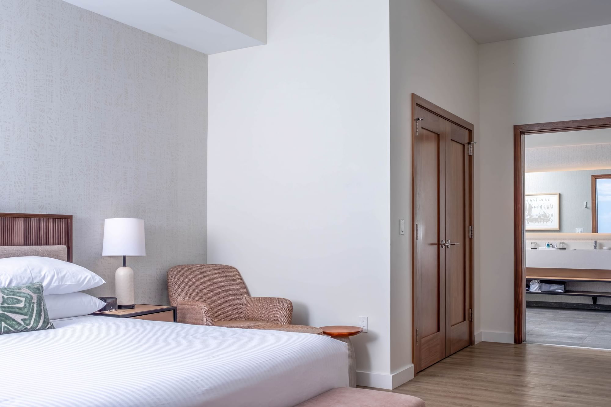 A hotel room with a king-sized bed, armchair, and doorway to bathroom