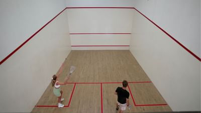 Two people playing squash on an indoor court with wooden flooring and red lines at Sugar Cane Club Hotel & Spa