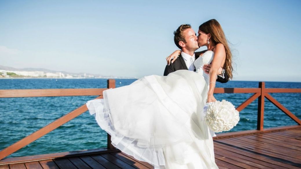 A wedded couple kissing on the pier at Marbella Club Hotel