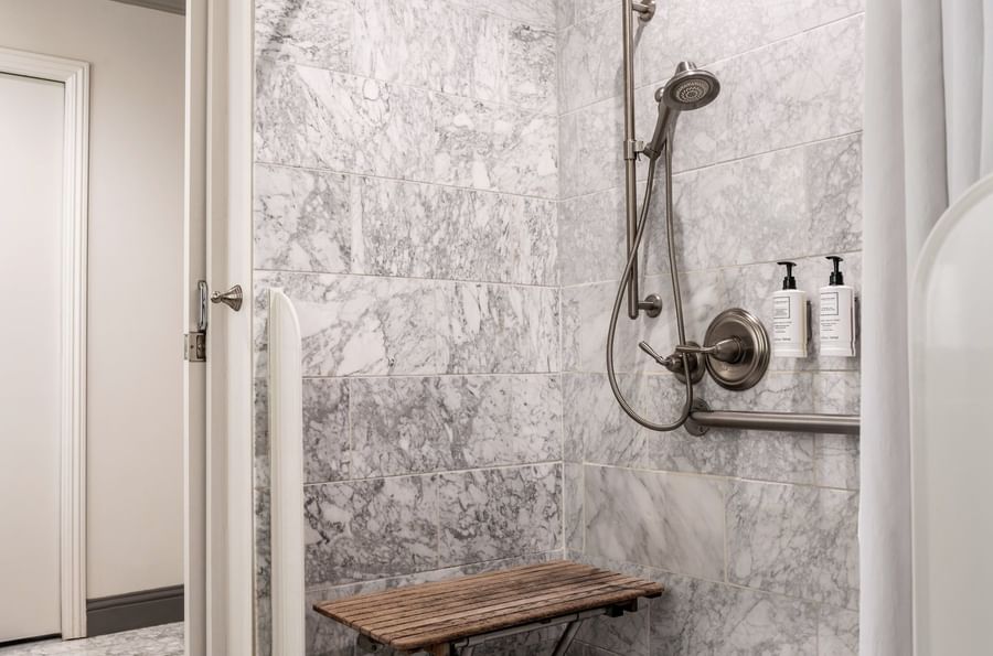 Walk-in marble shower with a wooden bench under a silver shower in Accessible Executive Front Suite at Warwick San Francisco