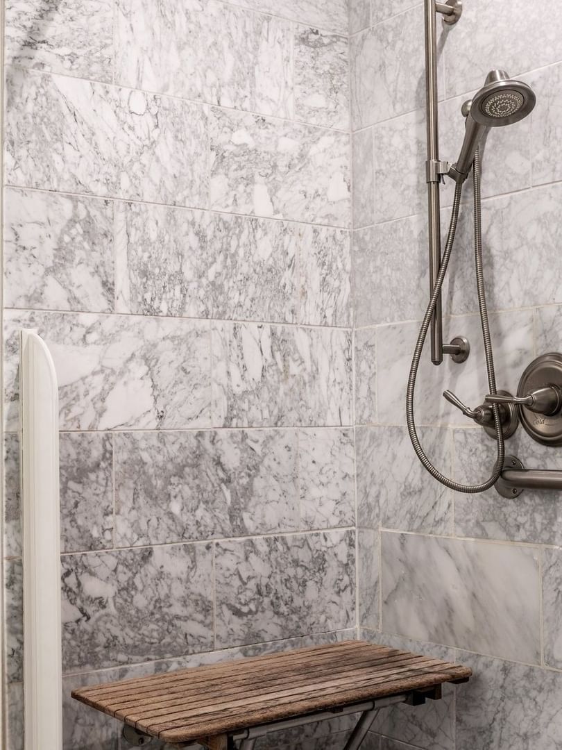 Walk-in marble shower with a wooden bench under a silver shower in Accessible Executive Front Suite at Warwick San Francisco