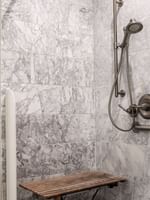Walk-in marble shower with a wooden bench under a silver shower in Accessible Executive Front Suite at Warwick San Francisco