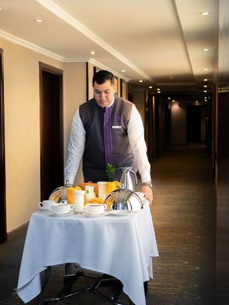 Hotel staff member pushing a room service trolley with breakfast through hallway at Saja Warwick Madinah