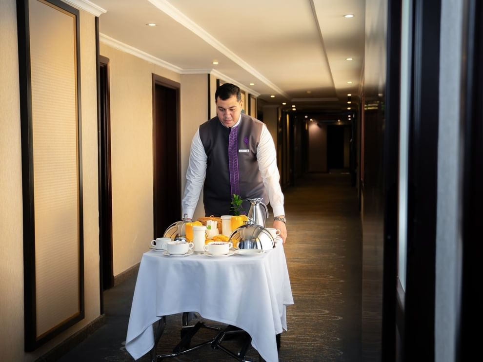 Hotel staff member pushing a room service trolley with breakfast through hallway at Saja Warwick Madinah