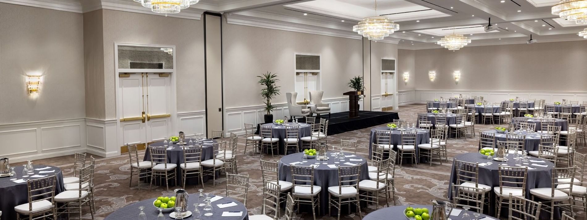 Round tables by silver chairs under crystal chandeliers in Turtle Creek Ballroom at Warwick Melrose Dallas