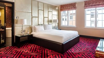 Modern Opium Suite at The May Fair Hotel, London with a king bed, ornate red and black carpet, and large windows
