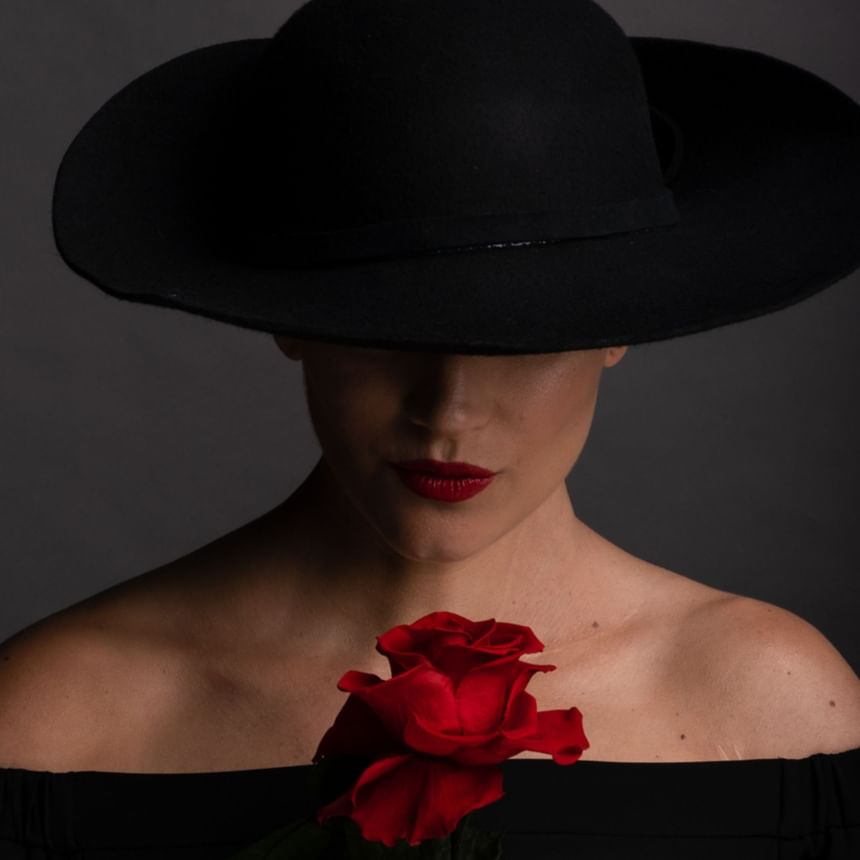Woman in a black hat holding a rose at Honeyrose Hotel